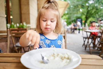 Little kid having breakfast at cafe. Adorable girl drinking still water, eating rice porridge with mango. enjoying breakfast. 