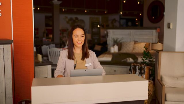 A Young Well Dressed Female Furniture Sales Person Walks Out From Behind a Counter to the Store Entrance and Smiles Taking a Deep Breath