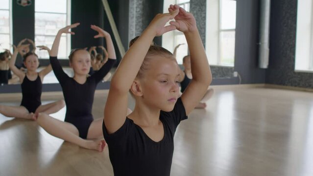 Little ballerinas in leotards doing warm up with hands over head while preparing for class in studio