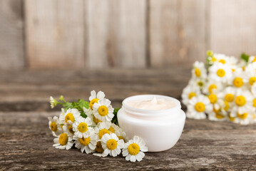Fototapeta na wymiar Open jar of cream for face, body and hands with chamomile flower on a wooden background. Herbal dermatological cosmetic hygiene cream. Natural cosmetic product. Beauty concept. Cosmetic tube.MOCKUP.