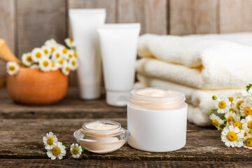 Fototapeta na wymiar Open jar of cream for face, body and hands with chamomile flower on a wooden background. Herbal dermatological cosmetic hygiene cream. Natural cosmetic product. Beauty concept. Cosmetic tube.MOCKUP.