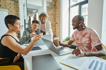 diverse business people discussing startup ideas and smiling near gadgets, coworking, leadership