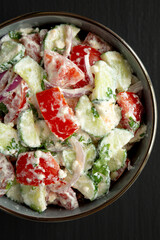 Homemade Tomato Cucumber Feta Salad in a Bowl on a black background, top view. Flat lay, overhead, from above.