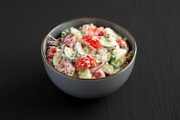 Homemade Tomato Cucumber Feta Salad in a Bowl on a black background, side view.