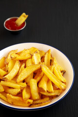 Homemade French Fries on a Plate on a black background, side view.