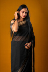 Portrait of a young beautiful girl wearing traditional black saree posing on a brown background.