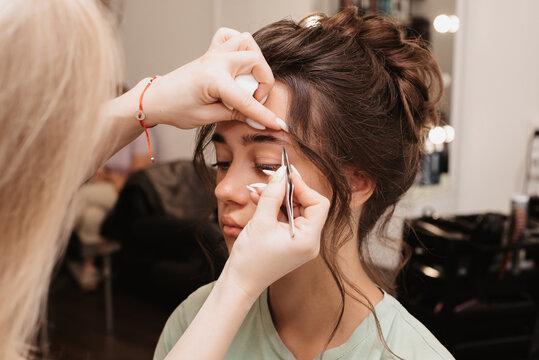 Shooting in a beauty salon. The master brow artist plucks out the hairs, giving the correct shape to the eyebrows of the model.