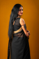 Portrait of a young beautiful girl wearing traditional black saree posing on a brown background.