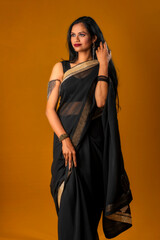 Portrait of a young beautiful girl wearing traditional black saree posing on a brown background.