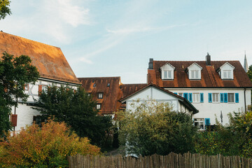 Fototapeta premium Old white cottage in cozy town. Street view landscape old city, little houses on sunset. Old architecture street front view. Calm old town street. Stone white pink rural cottages and summer gardens