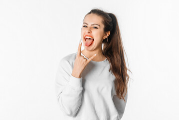 Crazy young woman showing tongue and rock and roll hand gesture, depicting heavy metal rock sign, posing in studio on white background