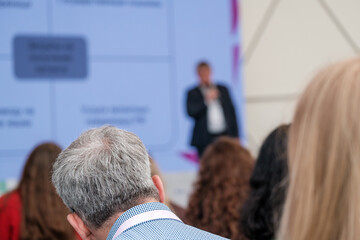 Back view of anonymous gray haired male in audience listening to presentation of speaker in...