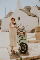 A young woman in a white dress and a white hat during tourist visit in Alberobello, Italy