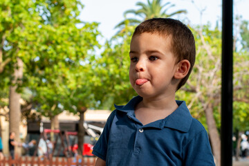 Niño pequeño sacando la lengua expresivo en la calle  - obrazy, fototapety, plakaty