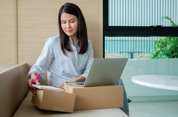 Happy young Asian woman entrepreneur, Smile for sales success after checking order from online shopping store in a laptop at home office, Concept of merchant business online and eCommerce