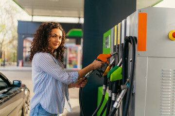 Young woman with curly hair refueling car at a self service gas station