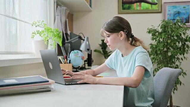 Preteen girl studying at home at her desk typing on laptop computer