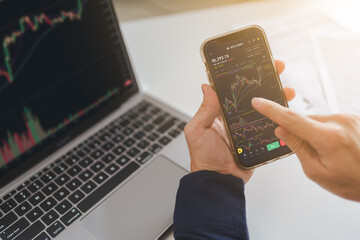 Trader, investor or businessman is pointing on smartphone, laptop on trading stock market graph, candlestick chart as Bitcoin Cryptocurrency price graph chart on screen. Investing money trader concept - 635884971