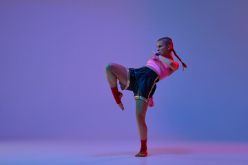 Obraz premium Dynamic photo of athletic teen girl, mma fighter in sportswear training against purple background in neon lights. Concept of mixed martial arts, sport, hobby, competition, athleticism, strength, ad