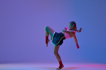 Dynamic photo of sportive teen girl, mma fighter in sportswear training against purple studio...