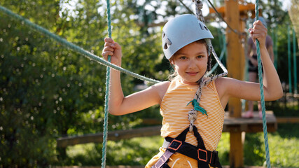 Little Girl Having Fun in a Rope Park Trail Facility. Happy little child enjoying climbing in an...