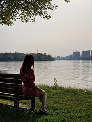 Girl tourist sits with her back on a bench on the river bank of the sea. Summer landscape with city view.
