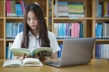 Portrait of an Asian girl college student studying in library doing project assignment and preparing for examination