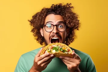 Foto op Aluminium Man eating a taco with curly hair glasses and green shirt isolated on yellow background © Poprock3d
