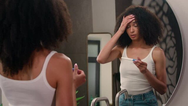 Worried scary afraid anxious African American woman girl in bathroom looking on positive pregnant test shocked unwanted pregnancy unplanned motherhood pregnant problem sad upset female holding head