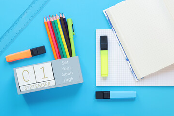 01 September. Image of a wooden calendar for September 1 on a blue table, top view. Back to school. Calendar, pencils and an open notebook. Stationery items