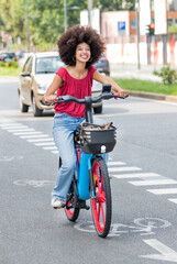 Smiling young ethnic woman riding electric bicycle on asphalt road in daylight