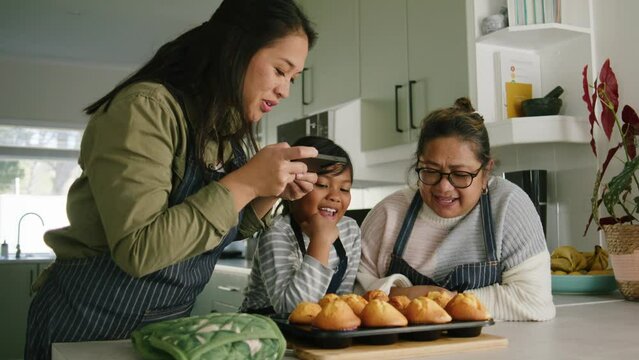 3 generation Asian African family baking together taking a photo of muffins , laughing smiling together