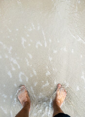 The barefoot on the clear beach with the white foam from the waves.