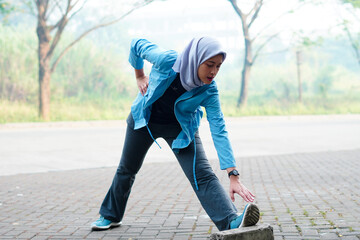 Beautiful Muslim woman working out outdoors in the morning. Sporty woman with a hijab warming up by...