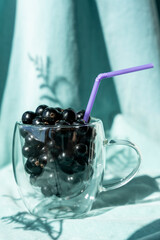 Summer fresh black currant berries in a glass mug with a cocktail tube 