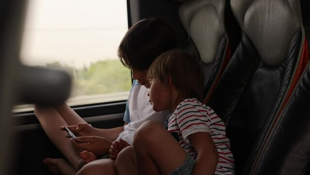 Children, siblings, playing on a mobile phone while traveling with bus on a long trip journey, family vacation