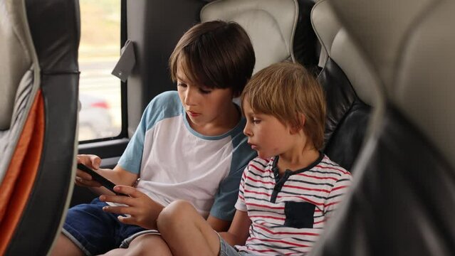 Children, siblings, playing on a mobile phone while traveling with bus on a long trip journey, family vacation