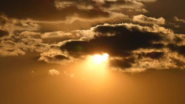 Sun passes through dramatic gray clouds on a golden sky during sunset