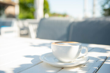 a cup of coffee with milk on a table on a sunny terrace with a gentle morning sun. freshness and calmness of the morning.