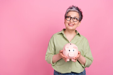 Fototapeta na wymiar Photo of dreamy pensioner business lady khaki trendy shirt hold piggy bank look empty space earn money isolated on pink color background