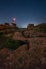 Persona en la noche subida a una roca con candil y castillo de fondo y meteorito