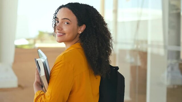 Positive trendy female student. Happy lovely brazilian or hispanic female student, with a backpack and notebooks in her hand, walks near the university campus, turns and smiles at the camera