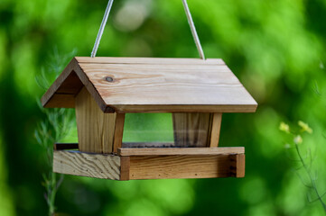Vogelfutterhaus aus Holz mit Haussperling und Spatz Vogelfütterung, Holzvogelhaus, Fütterung für Vögel, mit grünen Blättern im unscharfem Hintergrund