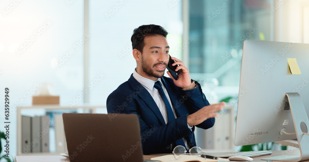 Fototapete Happy business man talking on his phone while working on a computer and smiling alone at work. Young corporate professional having a discussion and explaining project details to a colleague or client