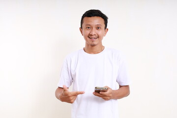 Happy asian funny man holding a cell phone while pointing on it. Isolated on white