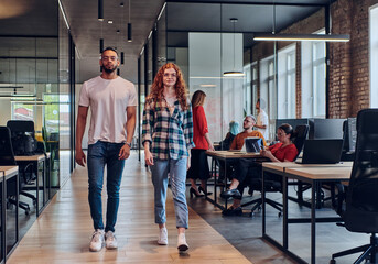 A young African American businessman and a modern businesswoman with orange hair stand side by...