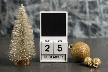 Wooden calendar with December 25 date and beautiful Christmas decoration on dark textured background with copy space