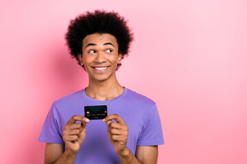 Photo of good mood man with afro hairstyle dressed blue t-shirt hold credit card look empty space offer isolated on pink color background