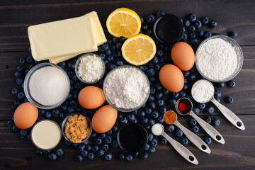 Blueberry Cobbler Cake Ingredients on a Dark Wood Table: Fresh blueberries, lemons, and other raw ingredients on a rustic wooden background