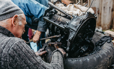 elderly man tuning a car engine at home in a garage, customizing an engine in a village.